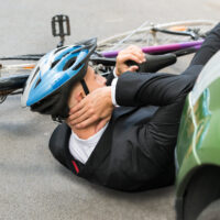 Male Cyclist With Neck Pain Lying On Street After Road Accident
